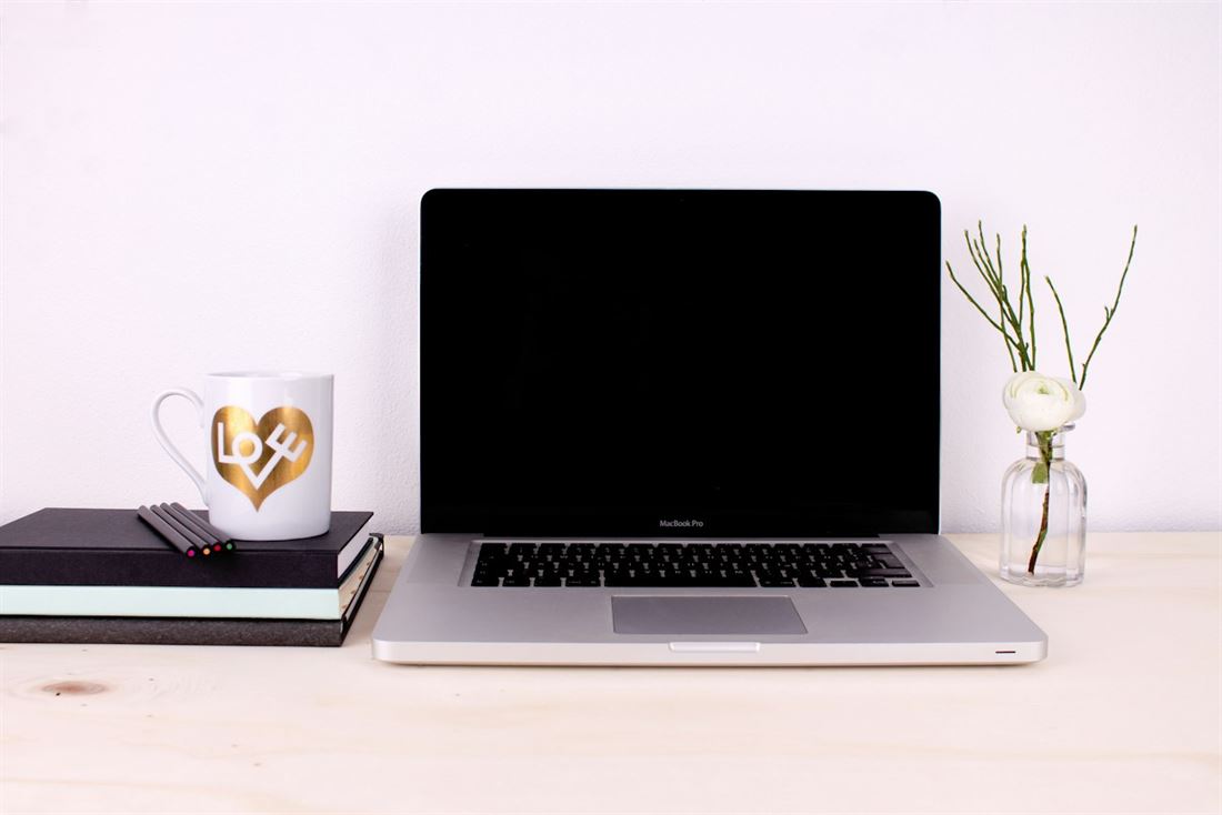 Heller Arbeitsplatz mit aufgeklapptem Laptop, Notizbuechern und einer Tasse